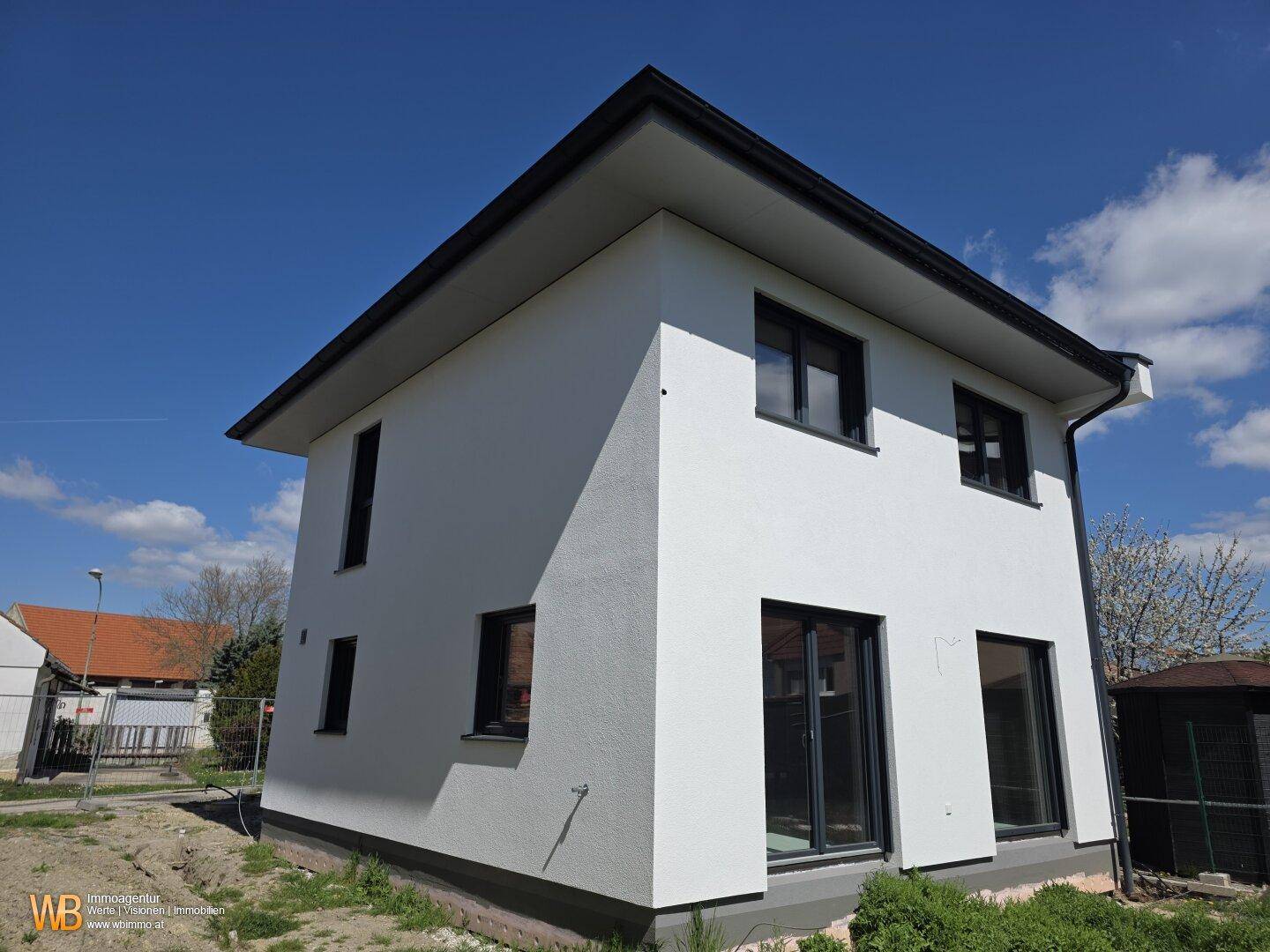 Modernes Einfamilienhaus in weißer Putzfassade mit dunklen Fensterrahmen und schrägem Dach.