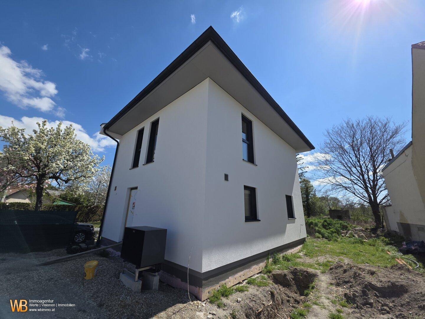 Seitenansicht eines neuen Einfamilienhauses mit weißer Fassade und umliegendem Grundstück.