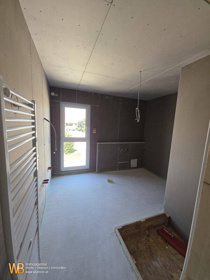 Badezimmer im Rohbau mit Fenster, vorbereiteten Anschlüssen und Handtuchheizkörper.