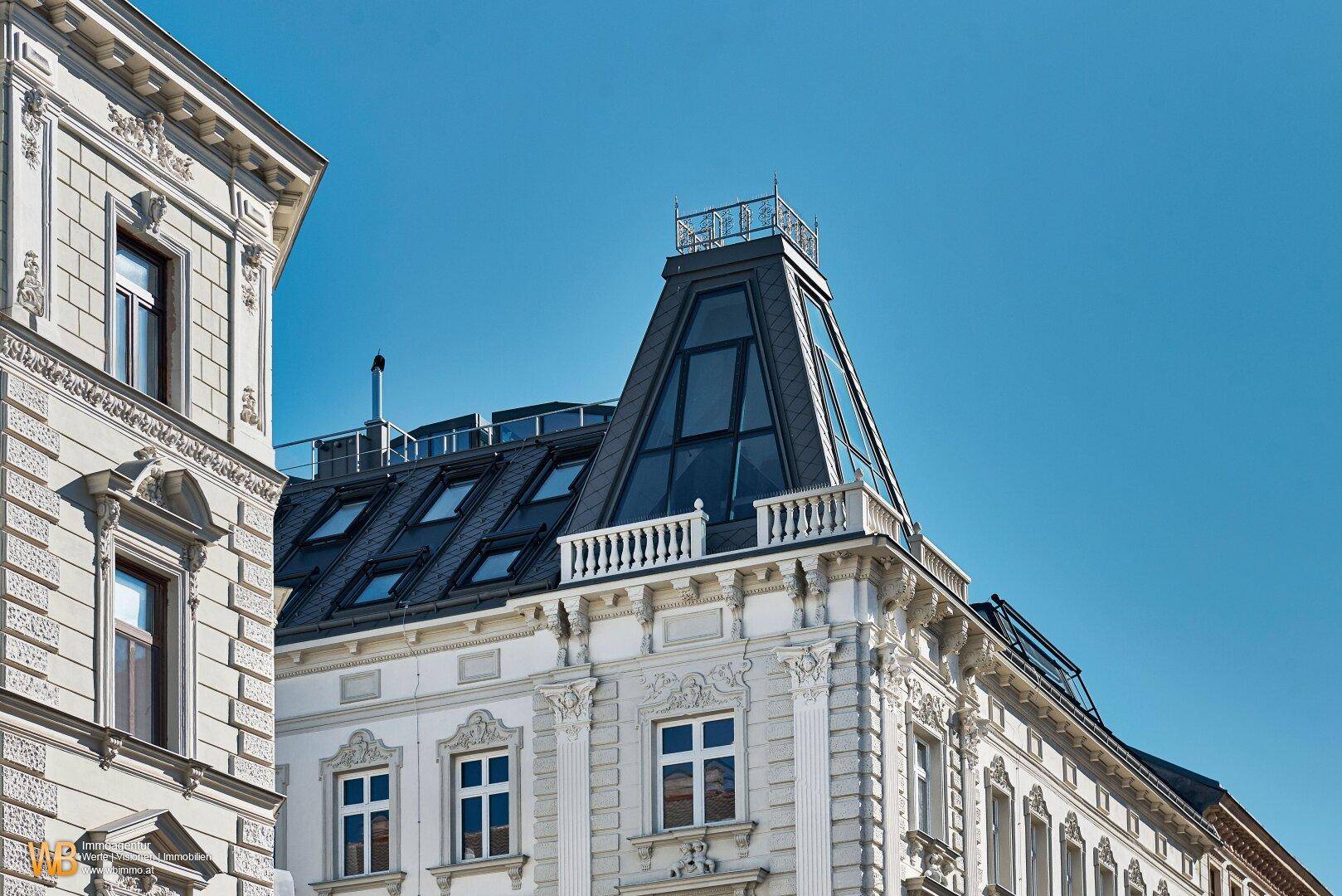 Moderner Dachausbau mit großen Glasflächen und Dachterrasse auf einem historischen Gebäude.