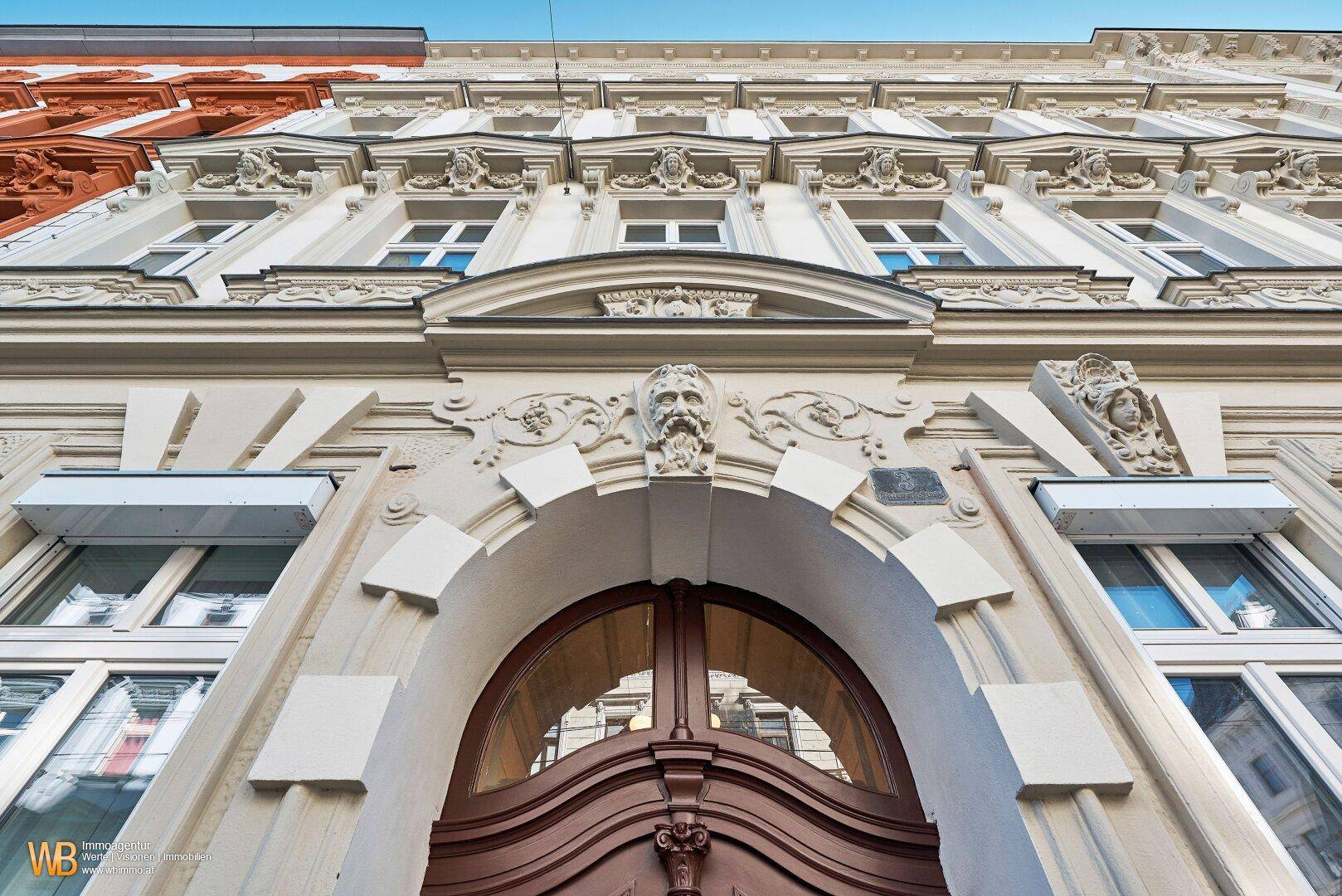 Historischer Gebäudeeingang mit Holztür und kunstvollen Stuckverzierungen an der Fassade.