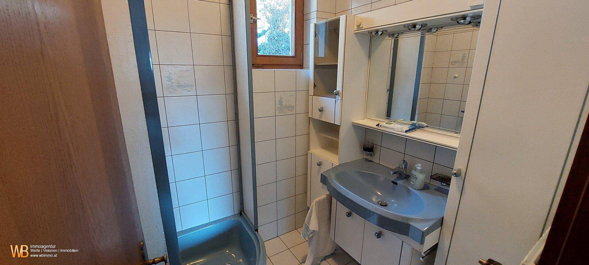 Funktionales Badezimmer mit hellblauen Fliesen, Waschbecken und Duschbereich, mit Fenster.