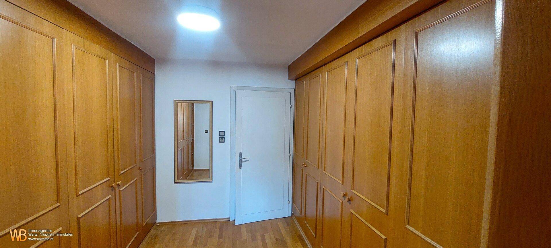 Geräumiger Flur mit durchgehenden Einbauschränken aus Holz und einem Spiegel, hell beleuchtet.