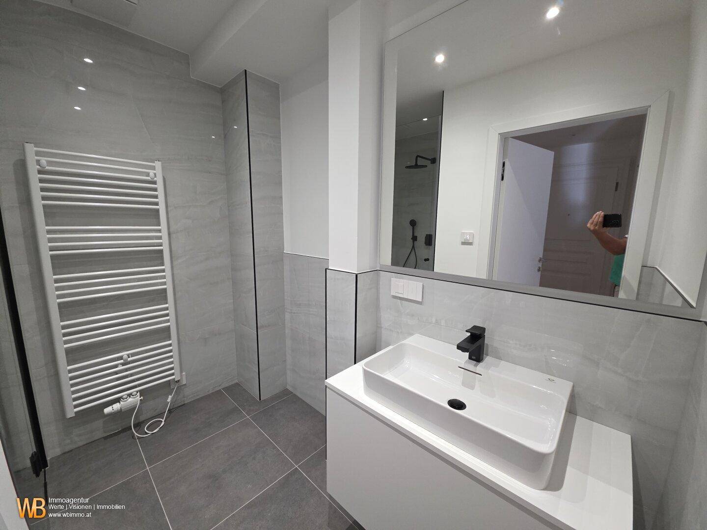 Modernes Badezimmer mit großem Spiegel, elegantem Waschbecken und praktischem Handtuchheizkörper.