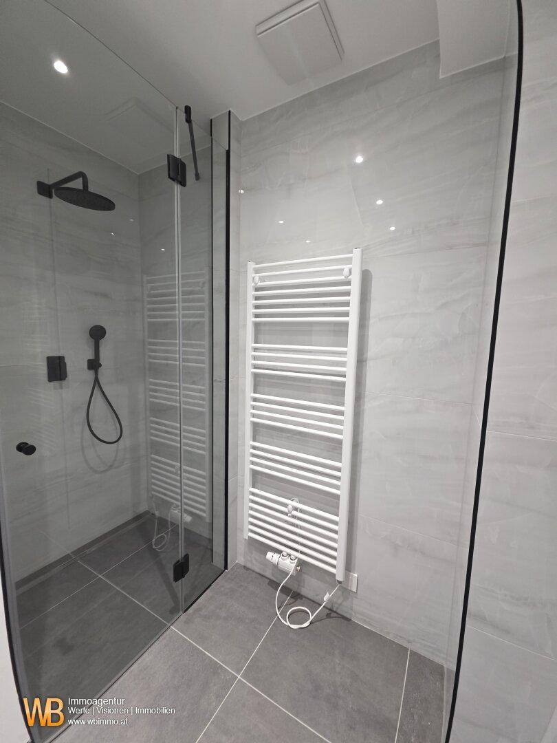 Duschbereich im modernen Badezimmer mit Glasabtrennung und beheiztem Handtuchhalter für Komfort.