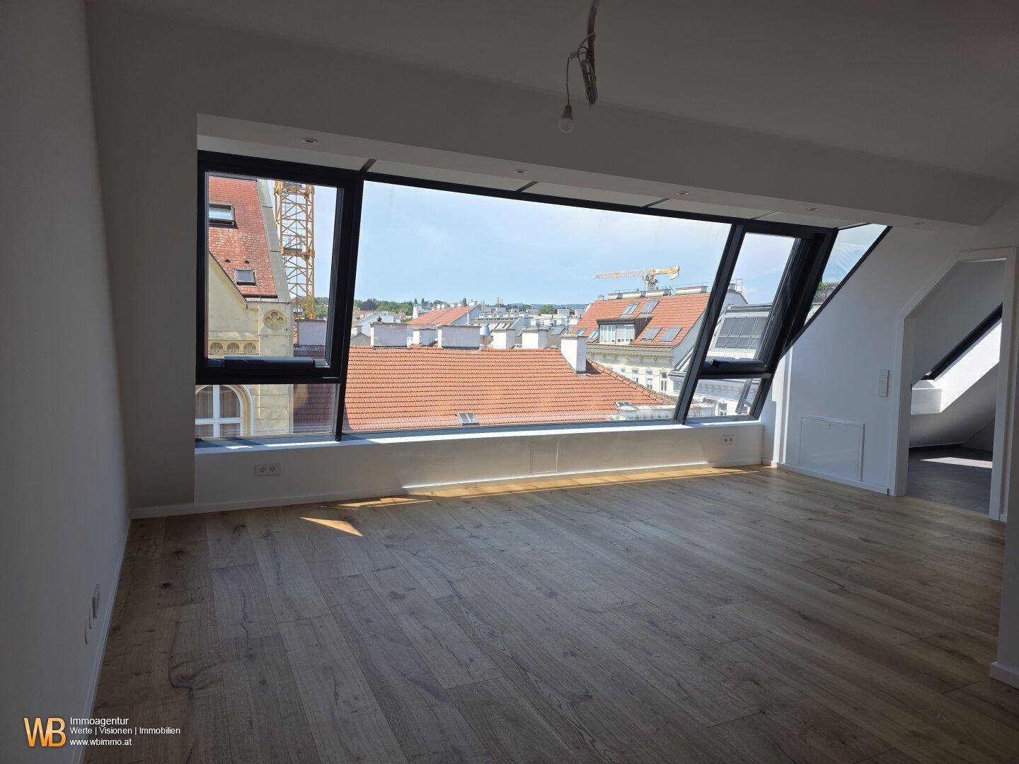 Geräumiger Wohnbereich mit Holzboden und großer Fensterfront, die einen weiten Stadtblick bietet.