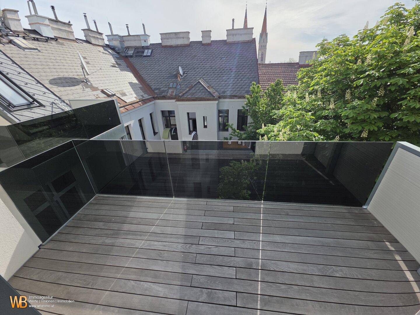Dachterrasse mit Holzboden und Glasgeländer, bietet einen malerischen Blick auf die Dächer der Stadt.