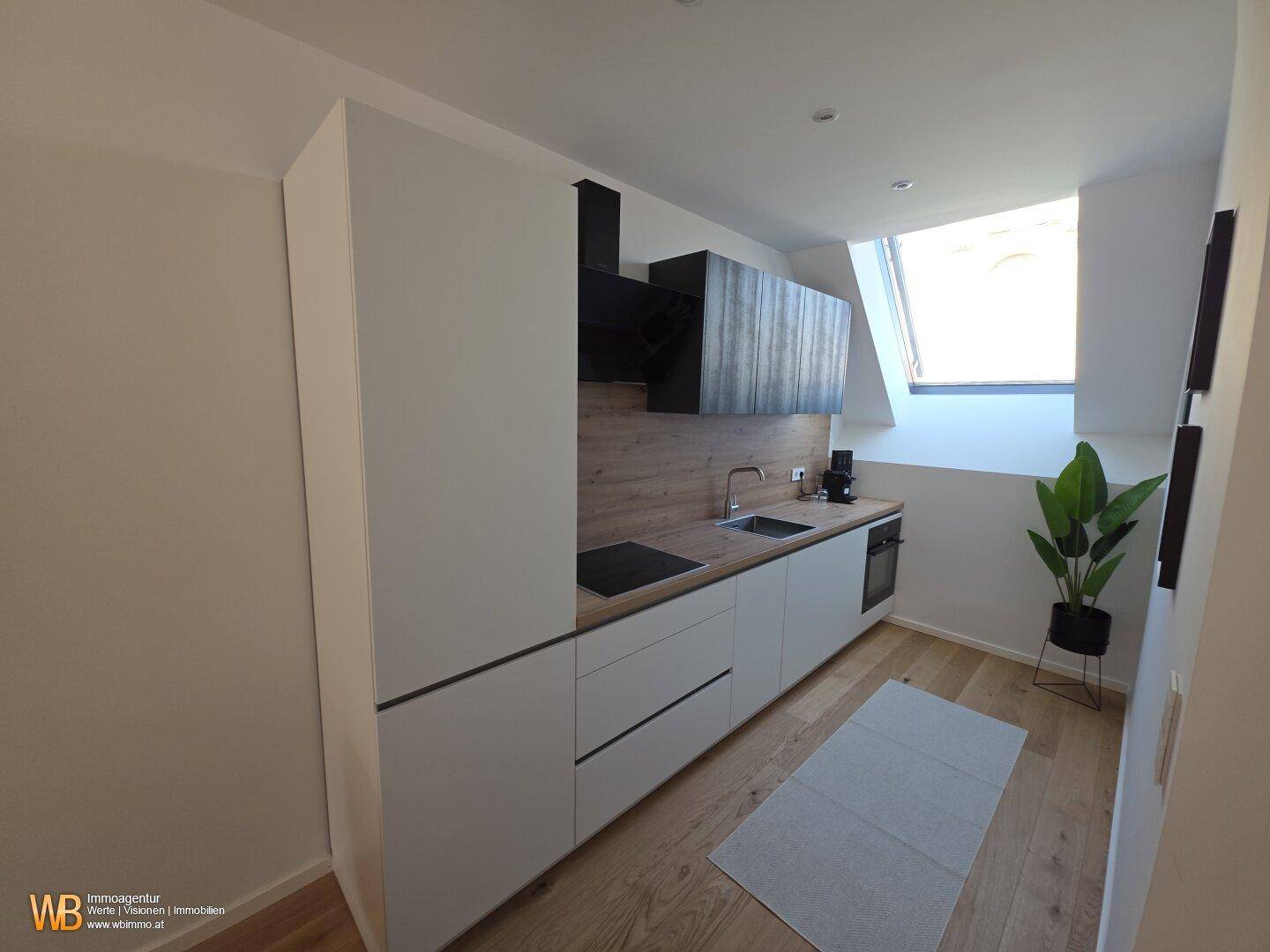Moderne Einbauküche mit weißen Fronten, Holzarbeitsplatte und Dachfenster für viel Tageslicht.