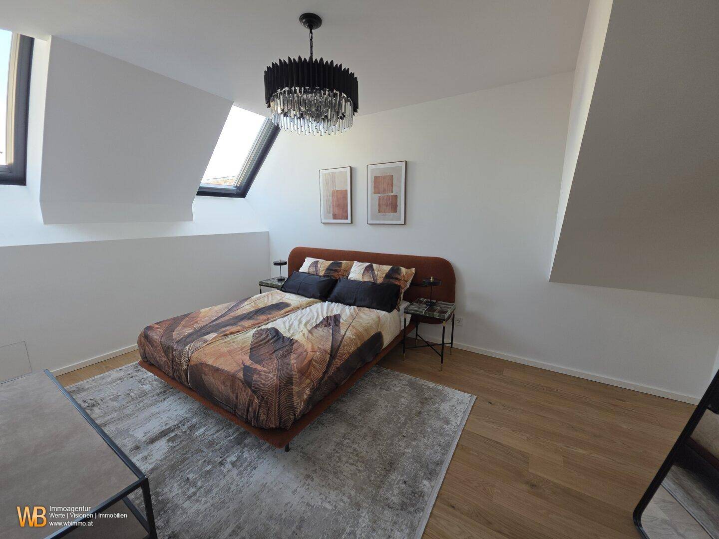Helles Schlafzimmer mit Holzboden, Dachschrägen und Dachfenstern, ausgestattet mit einem modernen Kronleuchter.