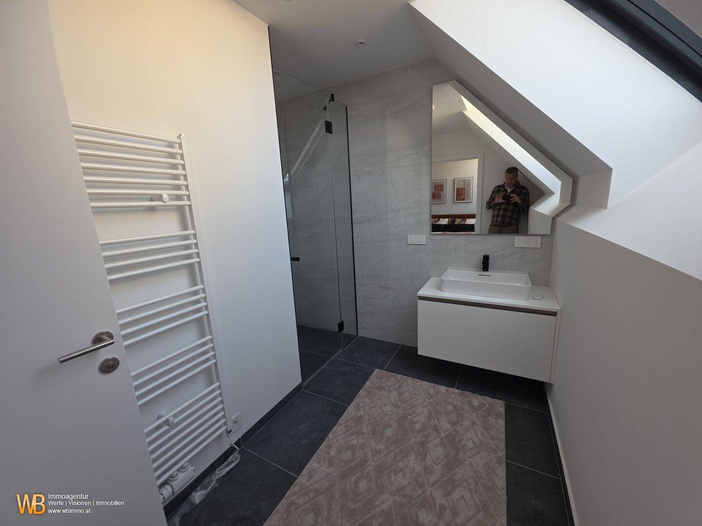 Modernes Badezimmer mit Waschbecken, Spiegelschrank, Handtuchheizkörper und begehbarer Dusche.