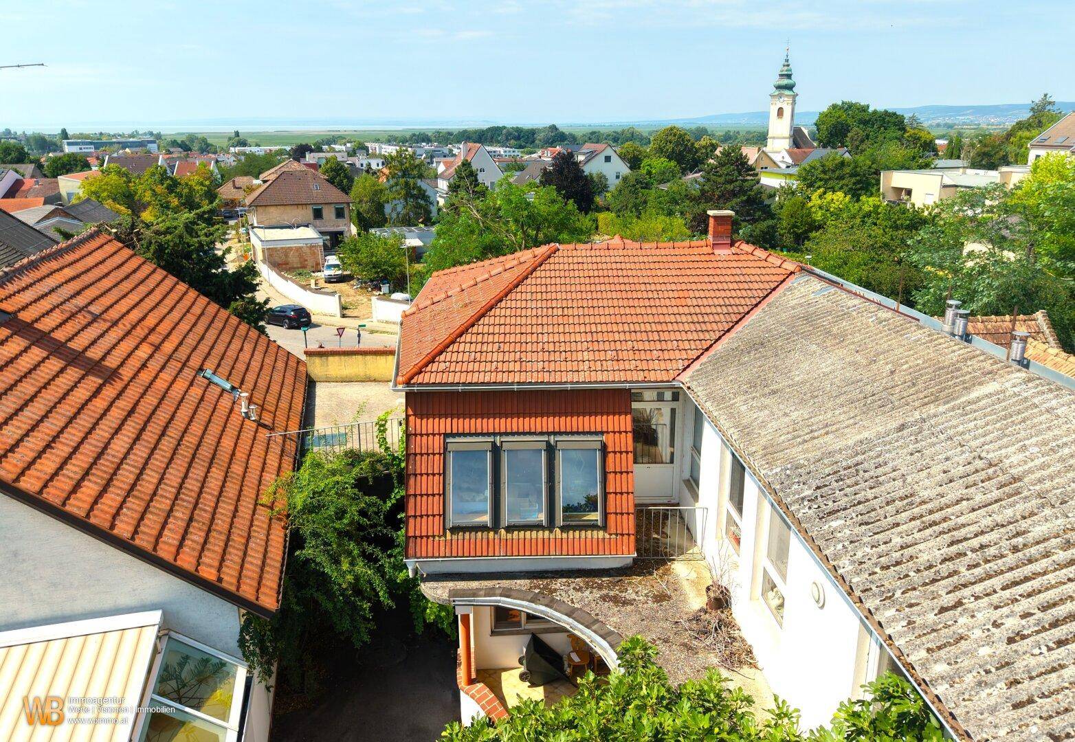 Luftaufnahme des Hauses mit Blick auf die umliegende Landschaft, Kirchturm und See in der Ferne.