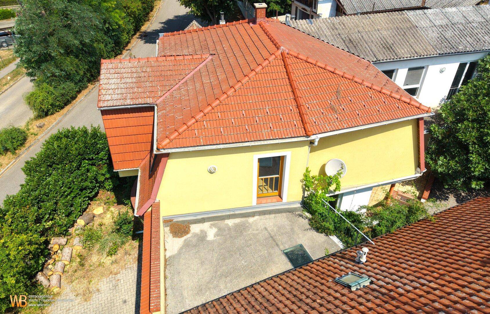Rückansicht des gelben Hauses mit rotem Ziegeldach und einer kleinen, unmöblierten Betonfläche.