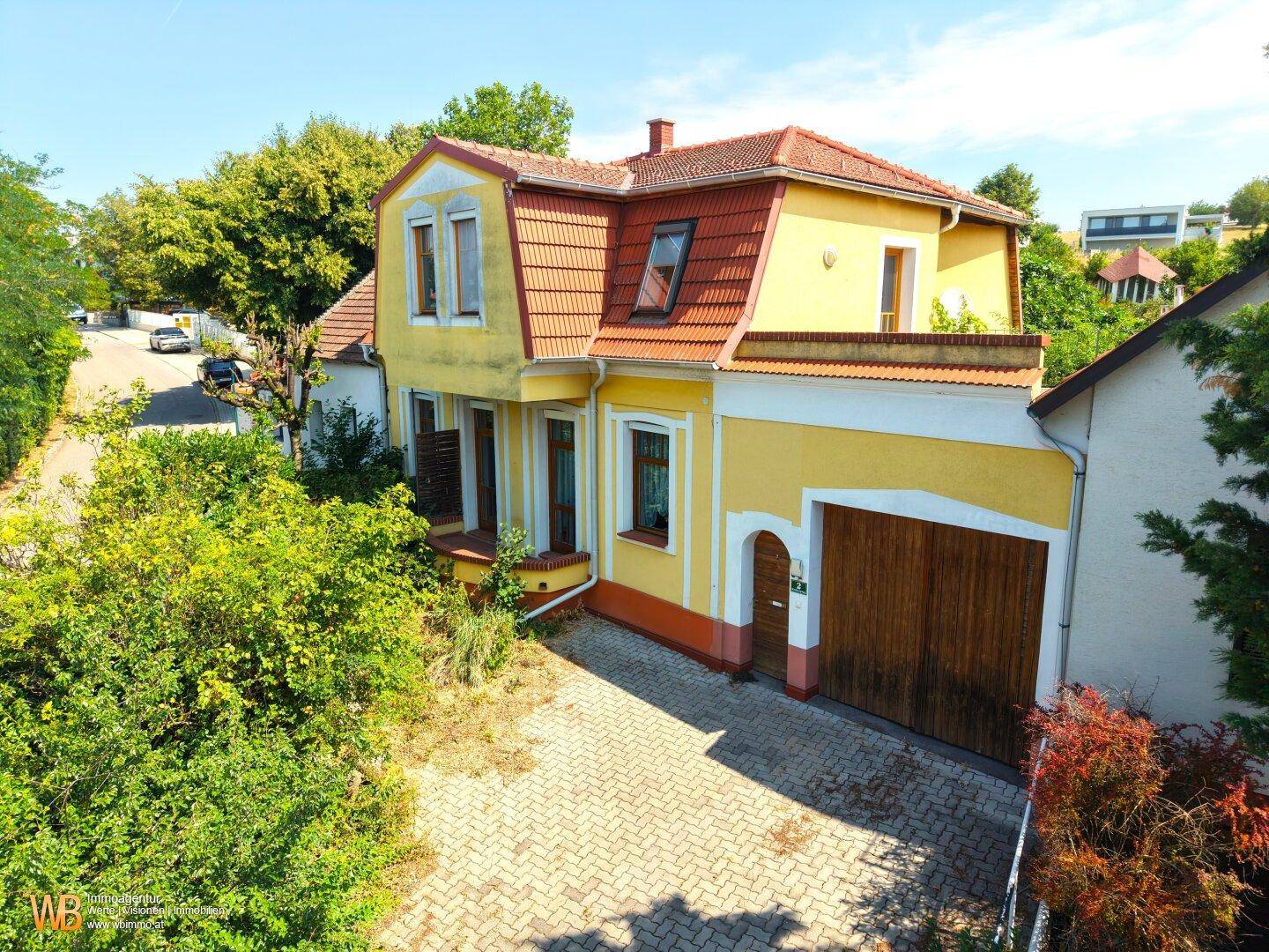 Vorderansicht des charmanten gelben Hauses mit rotem Dach, Garage und gepflasterter Einfahrt.