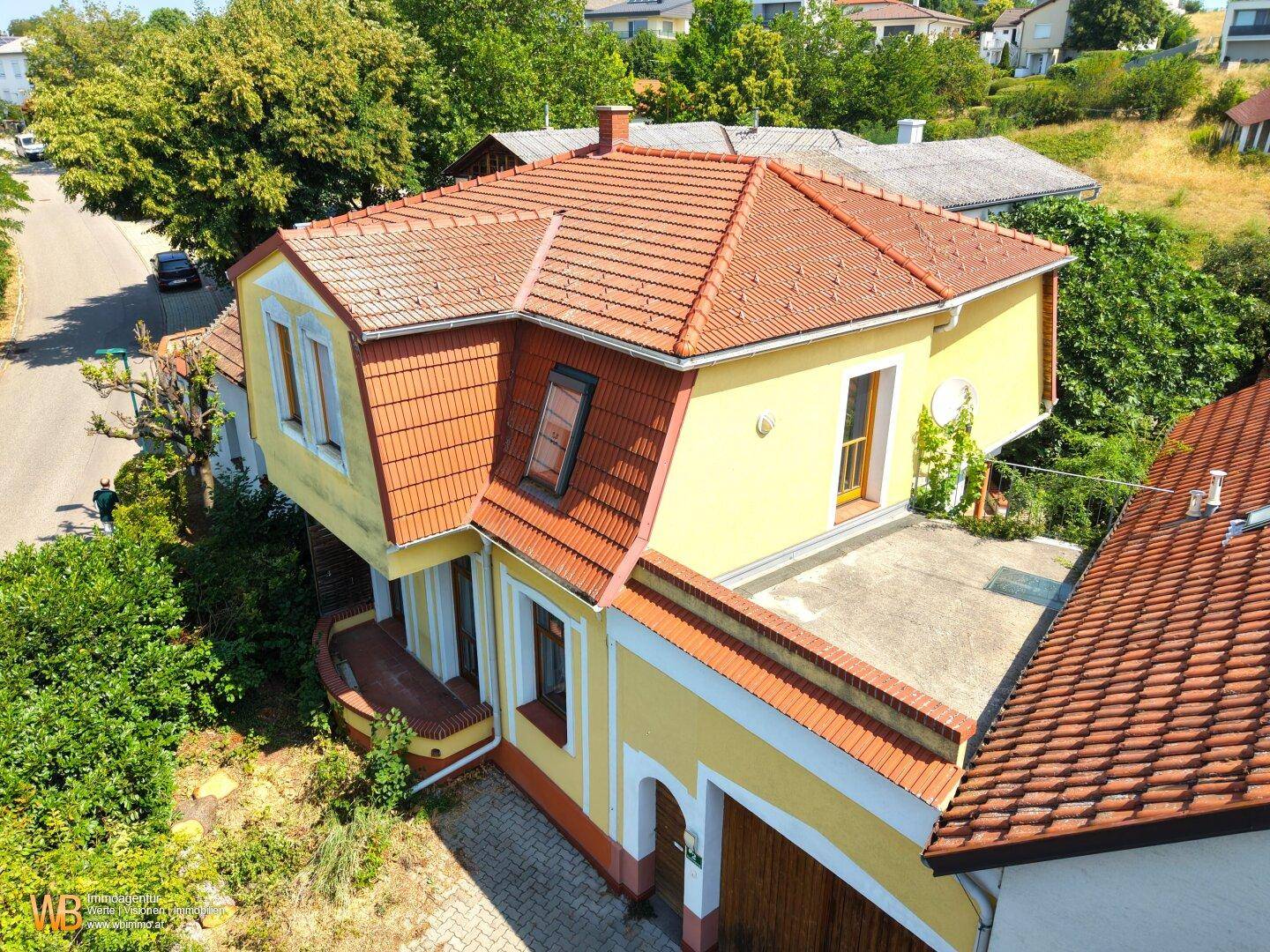 Gelbes Haus mit rotem Ziegeldach, Mansarddach und integrierter Garage in ländlicher Umgebung.