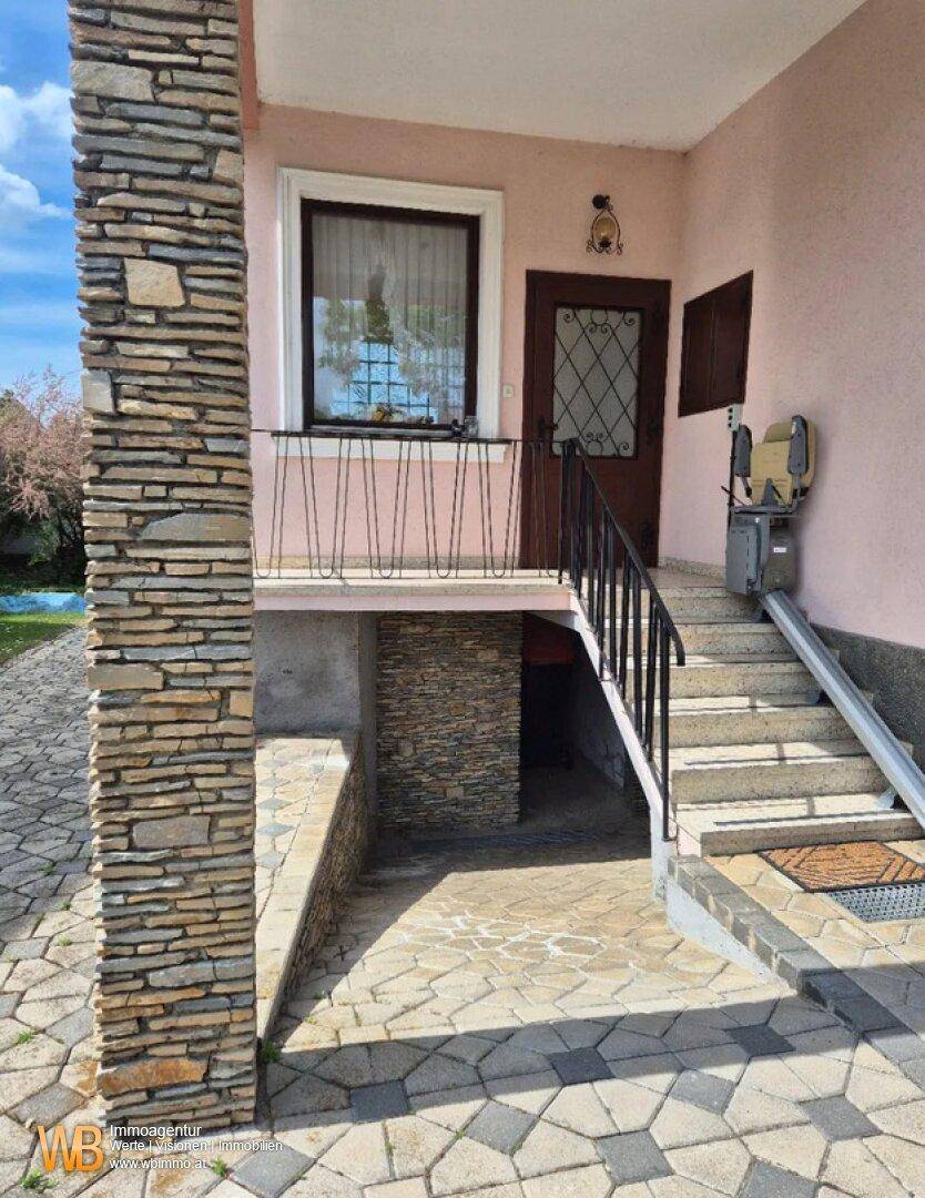 Eingangsbereich des Hauses mit Steinsäule, Treppe und einem Treppenlift für Barrierefreiheit.