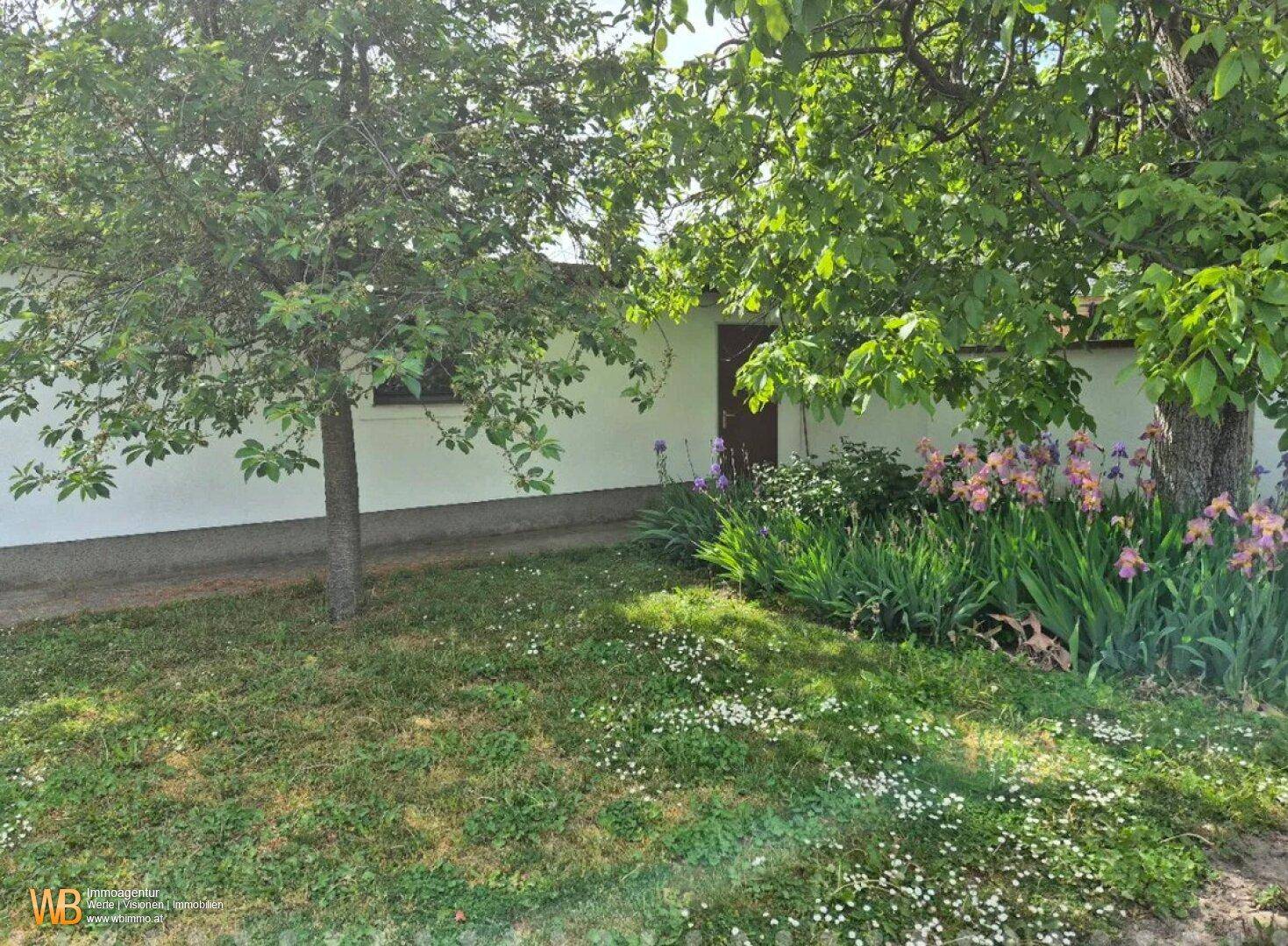 Gepflegter Gartenbereich mit Rasen, Bäumen und blühenden Blumenbeeten.