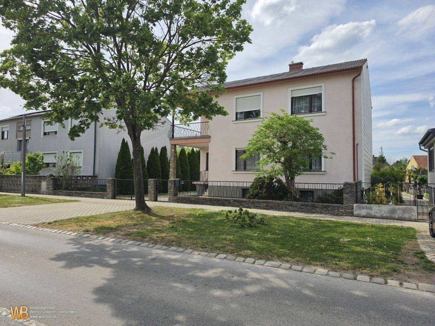 Seitenansicht des Hauses mit rosa Fassade, Fenstern mit Rollläden und einem gepflegten Vorgarten.