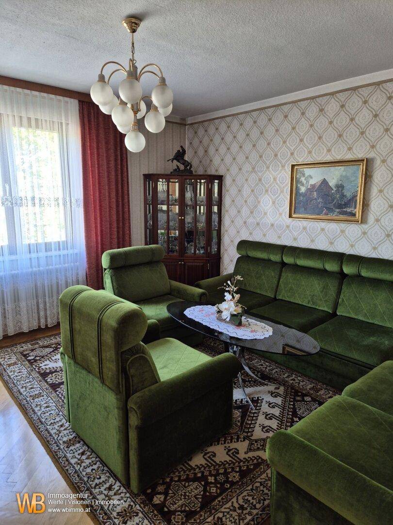 Klassisches Wohnzimmer mit grünen Polstermöbeln, gemusterter Tapete und Parkettboden.