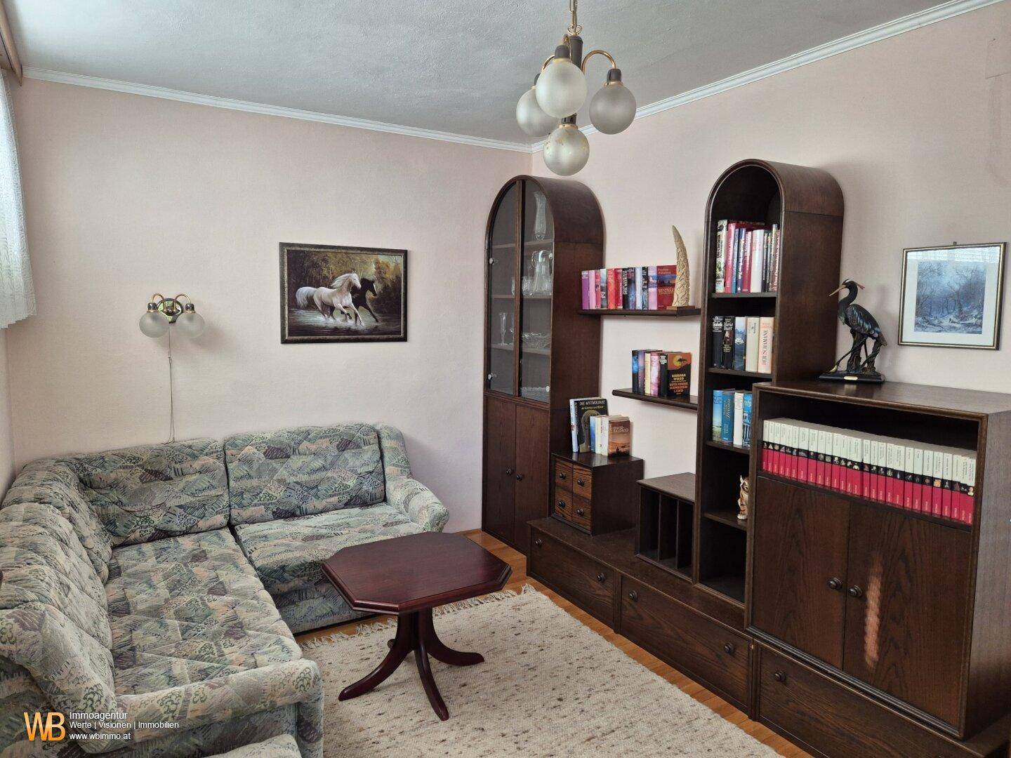 Gemütliches Wohnzimmer mit traditionellen Holzmöbeln, Sofa und Teppich, in warmen Farben gehalten.