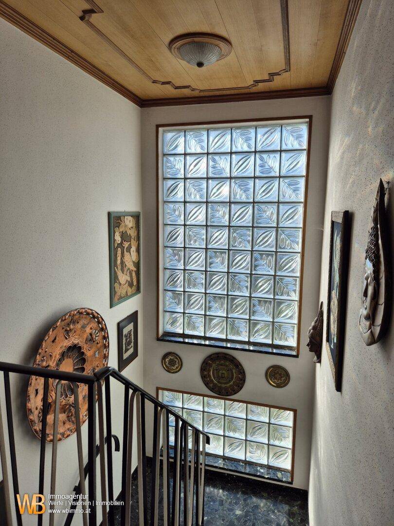 Treppenhaus mit Holzdecke, Glasbausteinfenstern und dekorativen Wandelementen, die viel Licht hereinlassen.