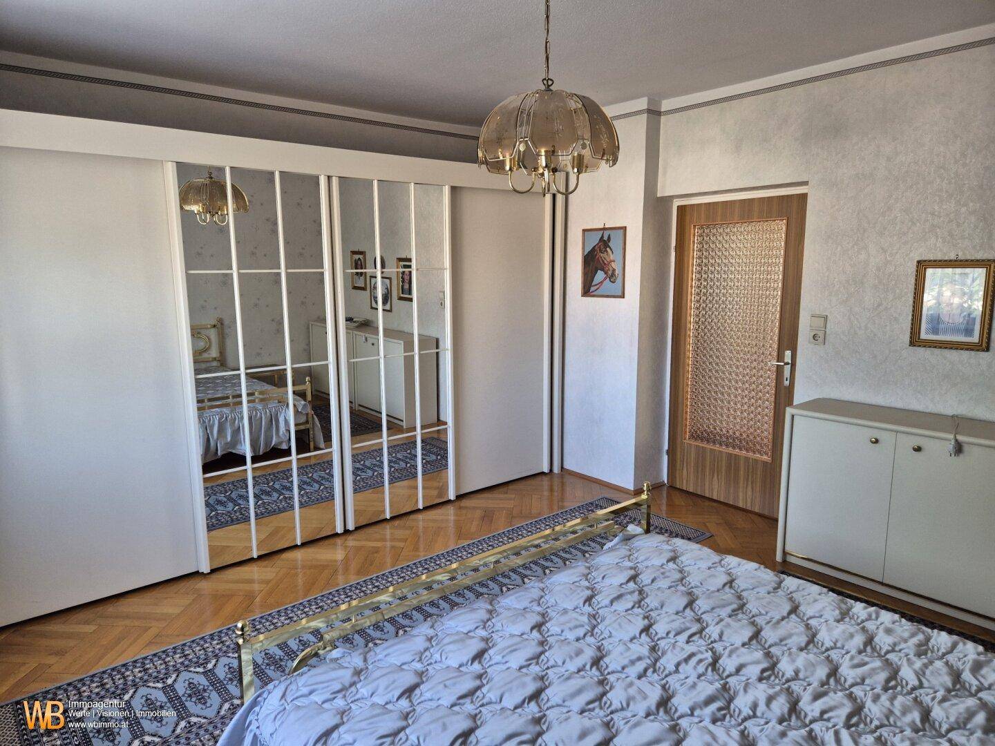 Schlafzimmer mit Spiegelschränken, Messingbett und Parkettboden, hell und geräumig.