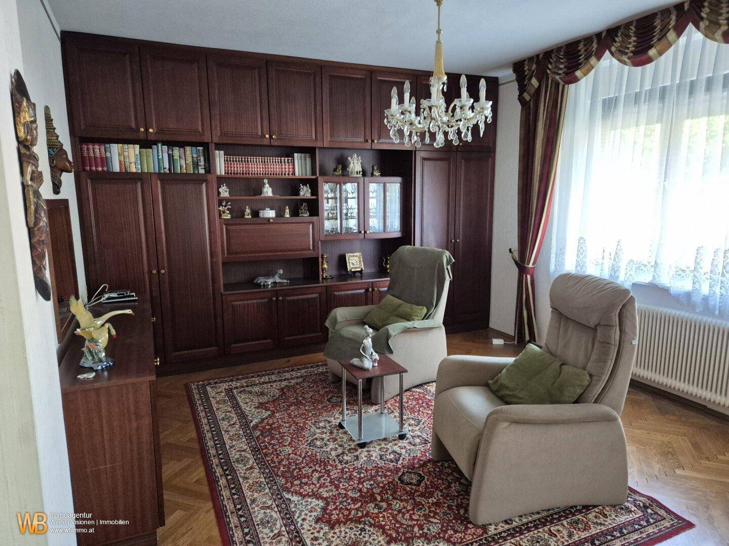 Arbeitszimmer mit großen Holzschränken, bequemen Sesseln und einem Kronleuchter.
