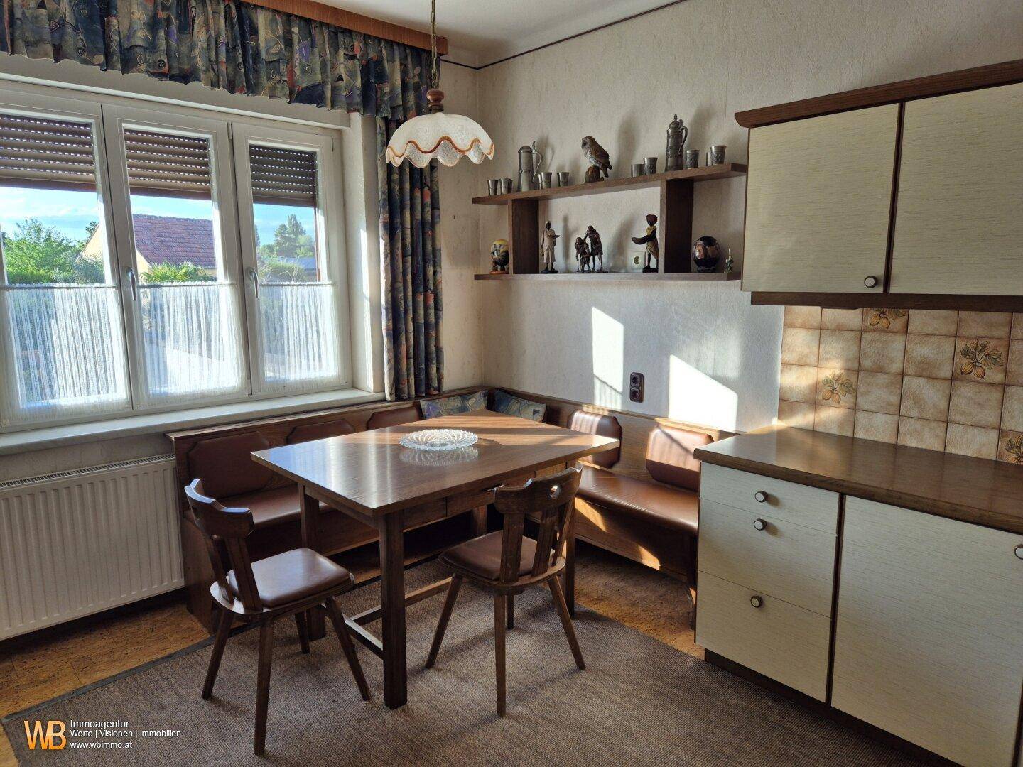 Traditionelle Wohnküche mit Holztisch, Eckbank und Blick ins Grüne durch das Fenster.