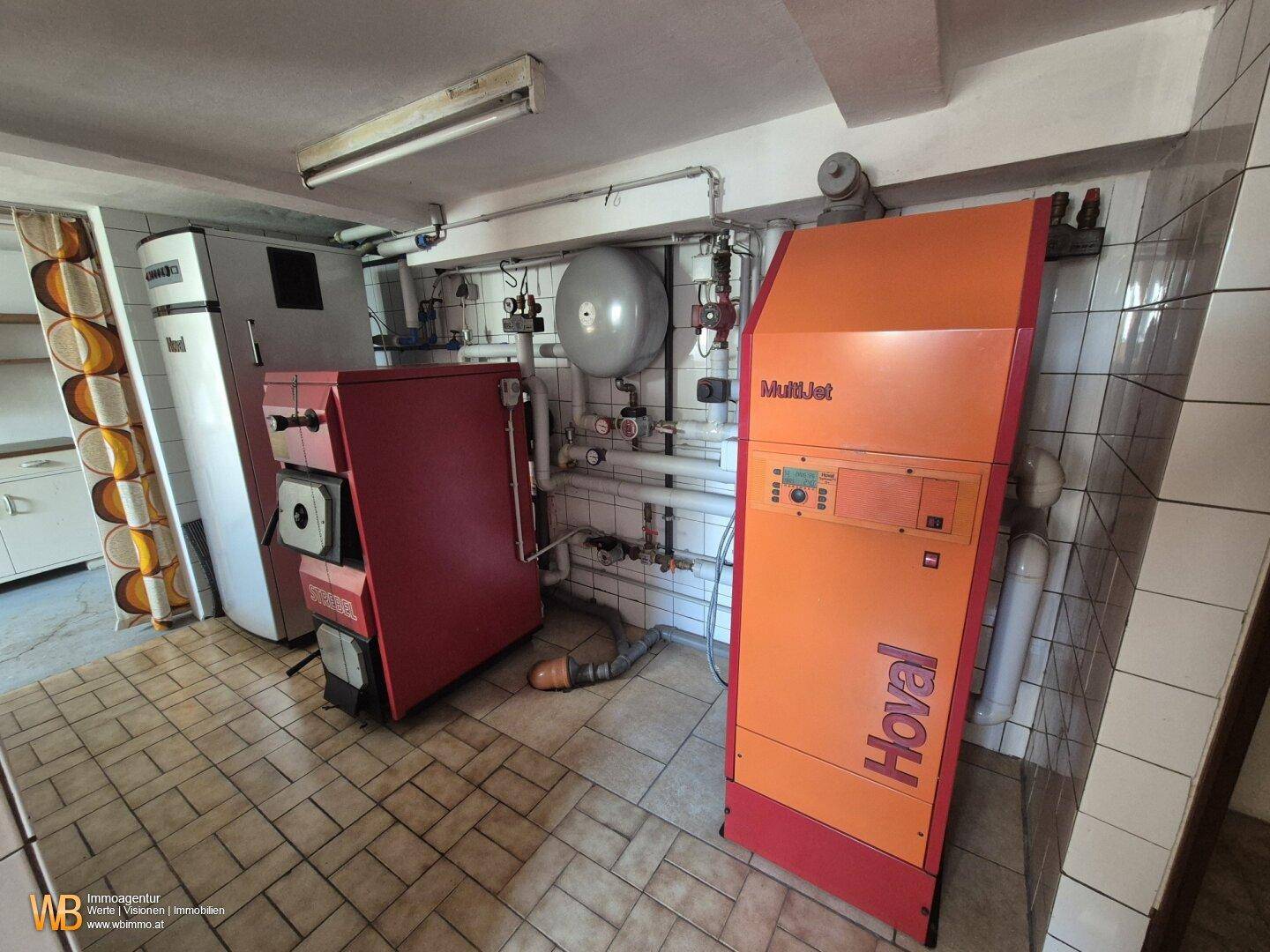Heizungsraum mit zwei großen Heizkesseln und technischen Installationen auf gefliestem Boden.