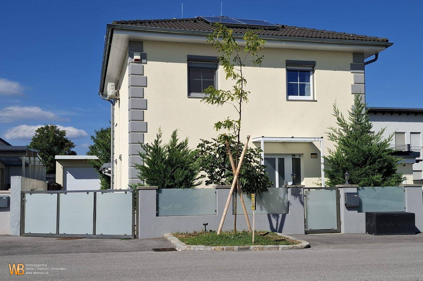Vorderansicht des Hauses mit moderner Architektur, gepflegtem Vorgarten und Photovoltaikanlage auf dem Dach.