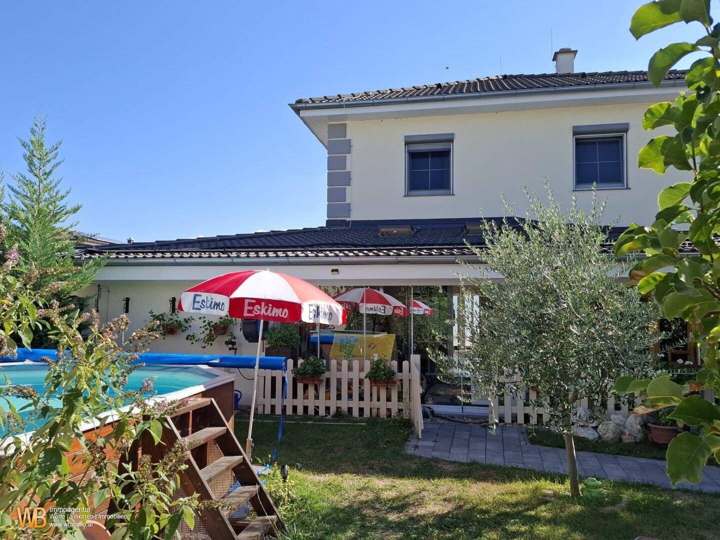 Sonniger Außenbereich mit Swimmingpool, Liegewiese und Blick auf das Einfamilienhaus.