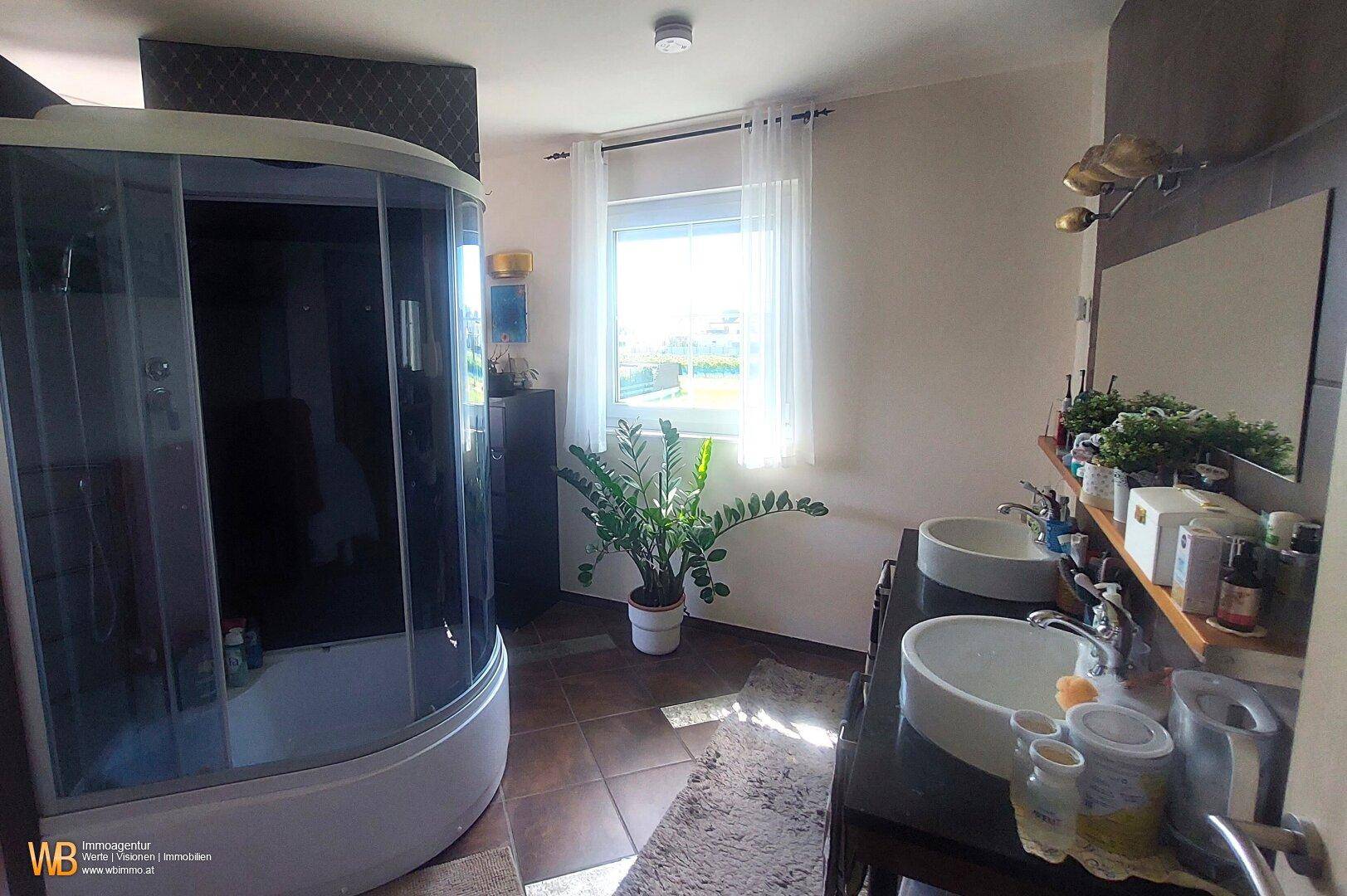 Helles Badezimmer mit Eckduschkabine, Doppelwaschbecken und Fenster für natürliche Belüftung.