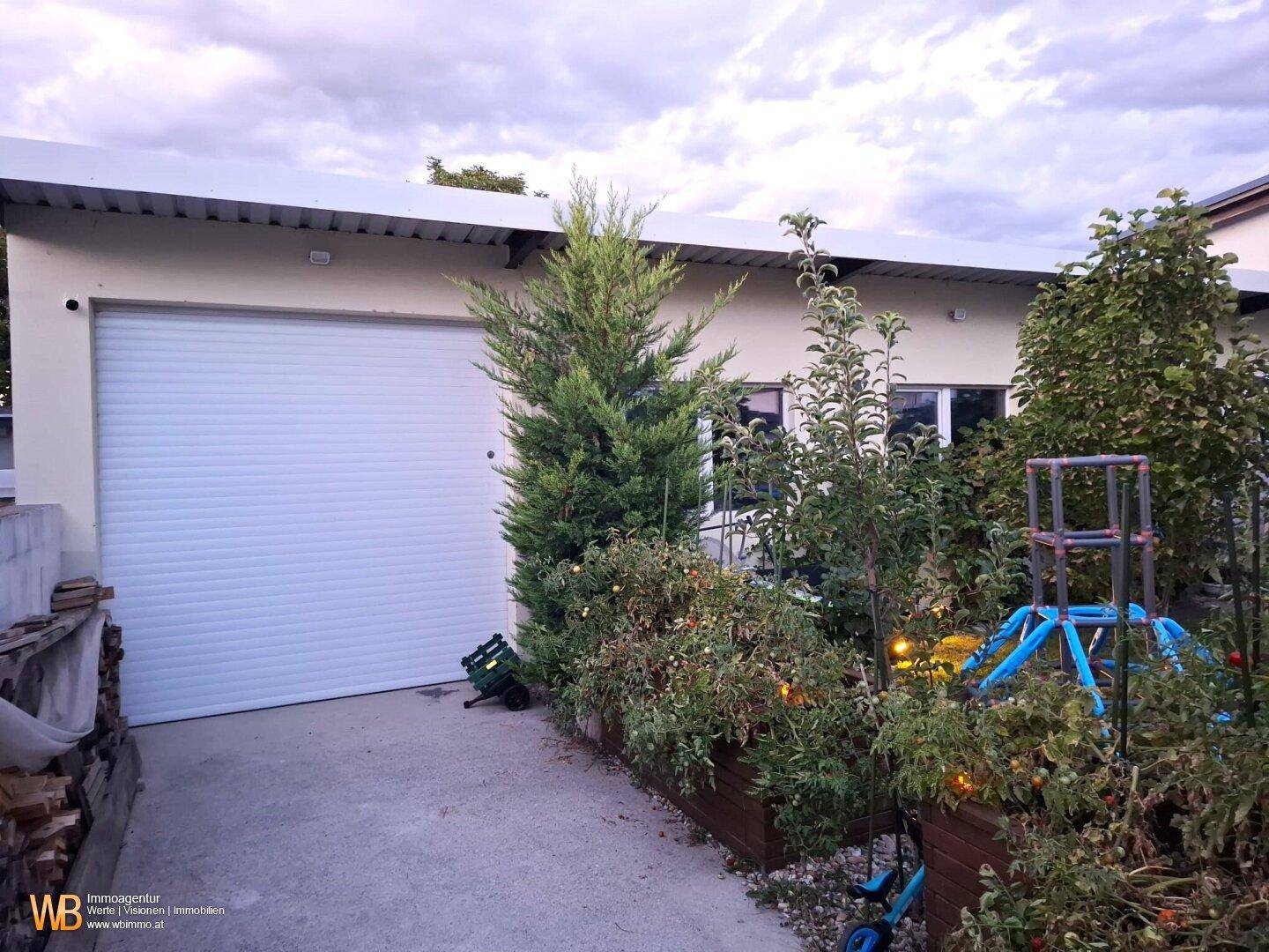 Geräumige Garage mit Rolltor und angrenzenden bepflanzten Hochbeeten im Außenbereich.