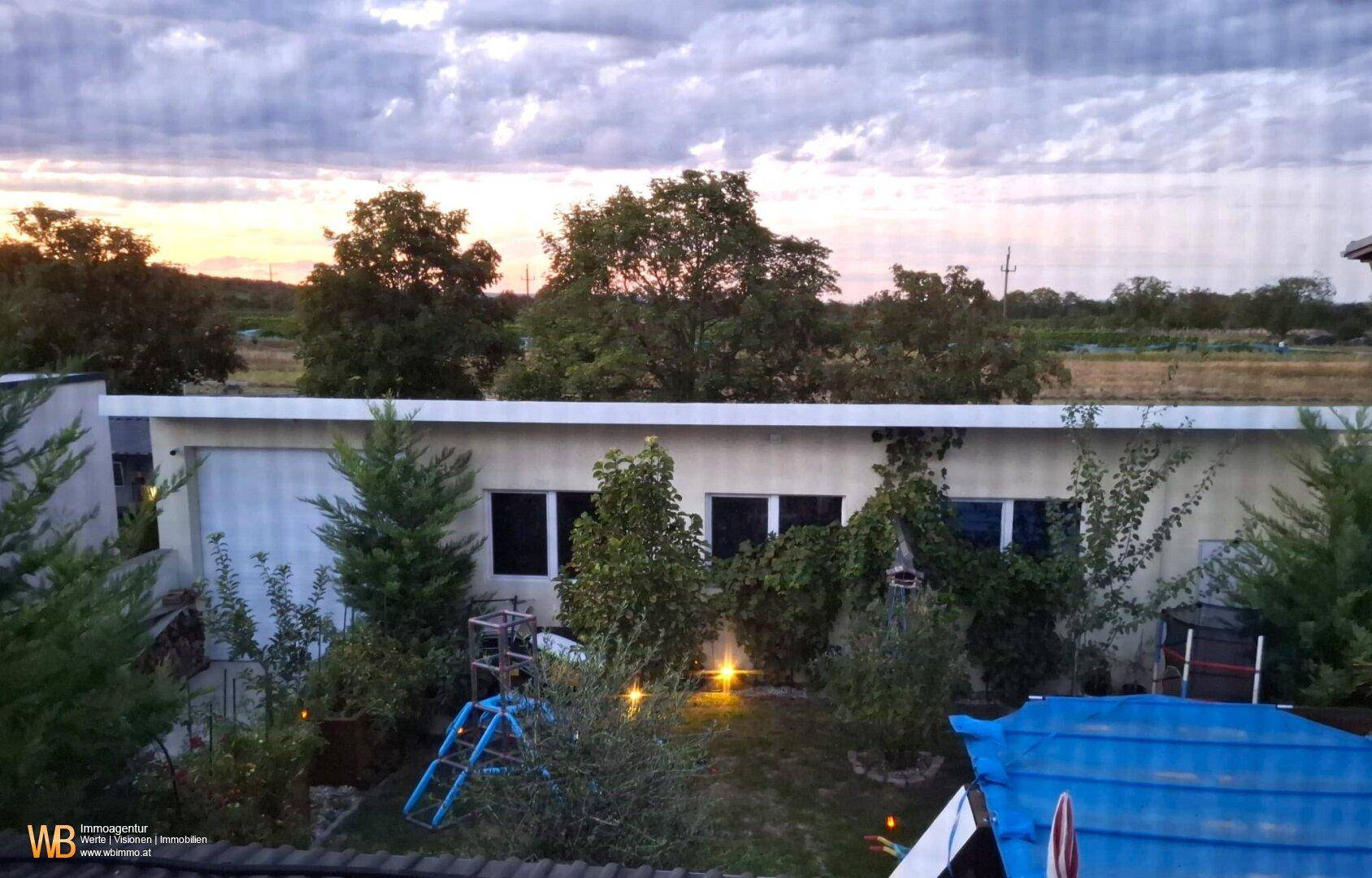 Gartenbereich am Abend mit üppiger Bepflanzung, Spielgeräten und Blick in die weite Landschaft.