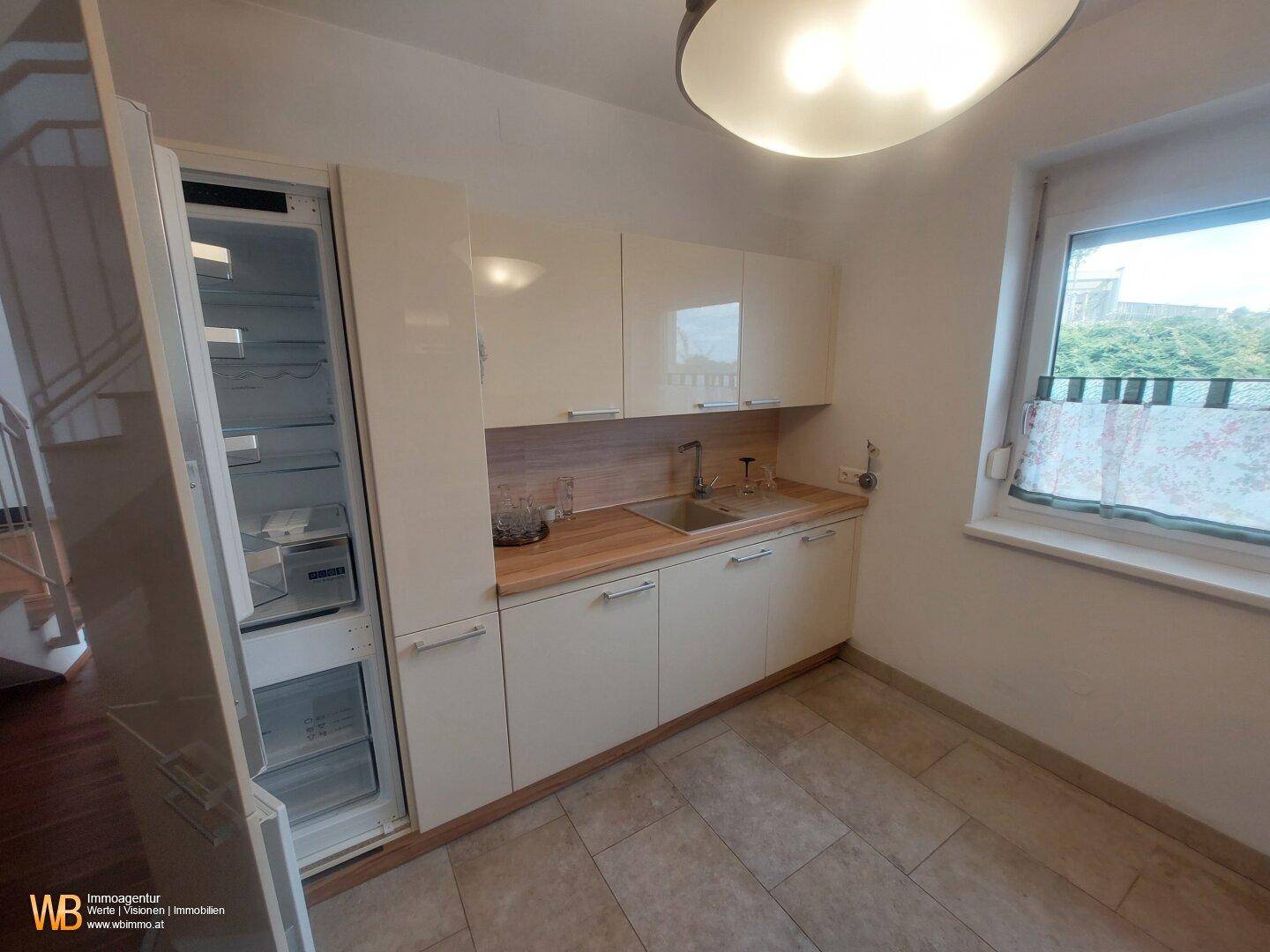 Helle Einbauküche mit beigen Hochglanzfronten, Holzarbeitsplatte und integriertem Kühlschrank.