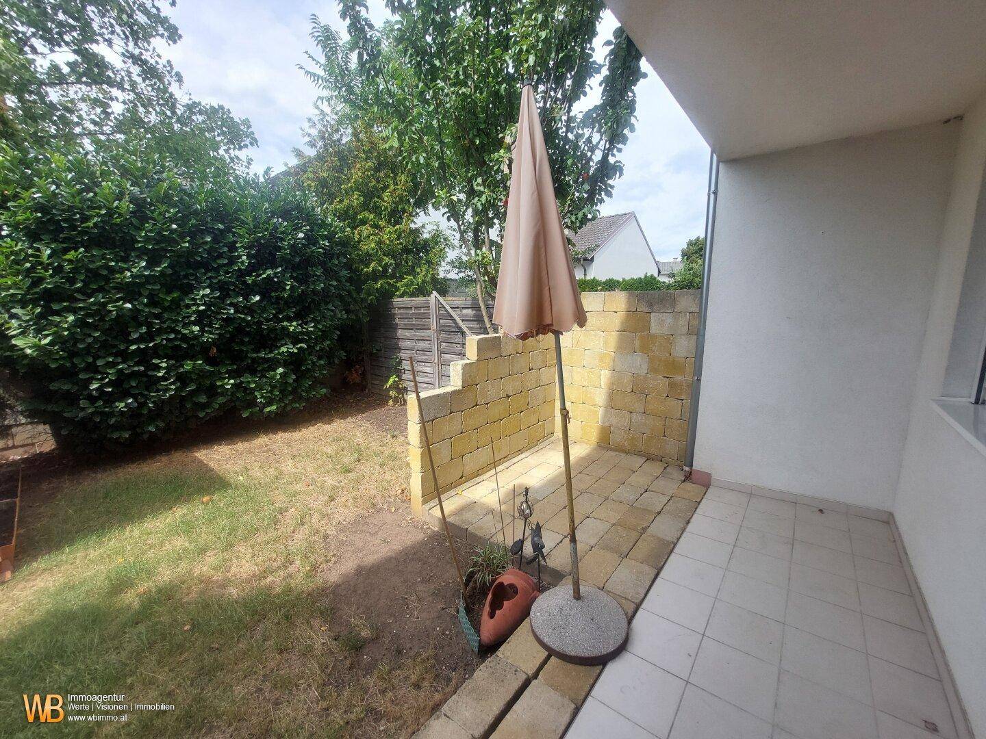 Gedeckte Terrasse mit Fliesenboden, Sonnenschirm und angrenzender Rasenfläche.