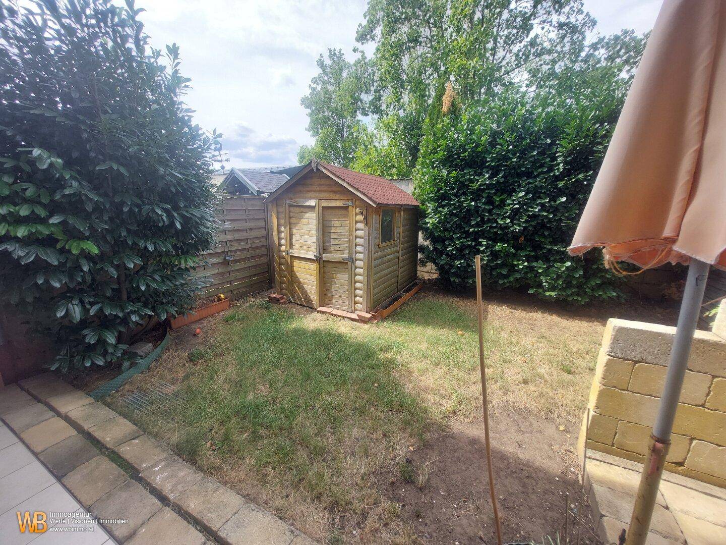 Kleiner Gartenbereich mit Holzschuppen, Rasenfläche und grünen Hecken.