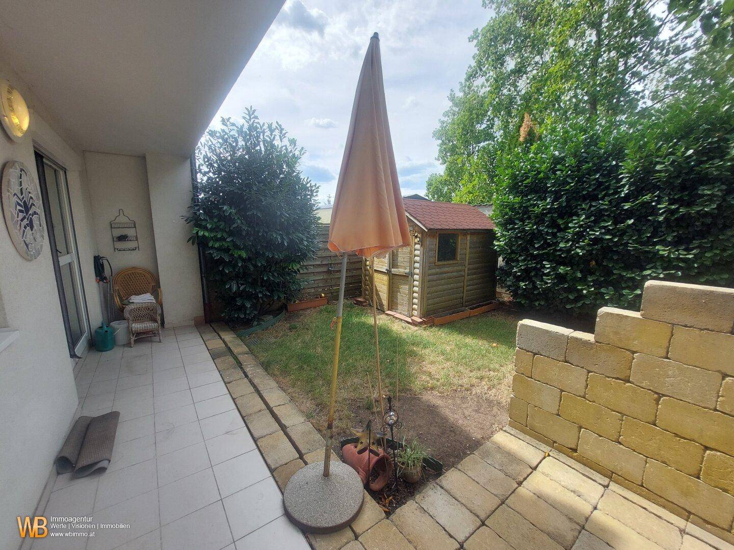 Terrasse mit Sonnenschirm und Blick auf den kleinen Garten mit Holzschuppen.