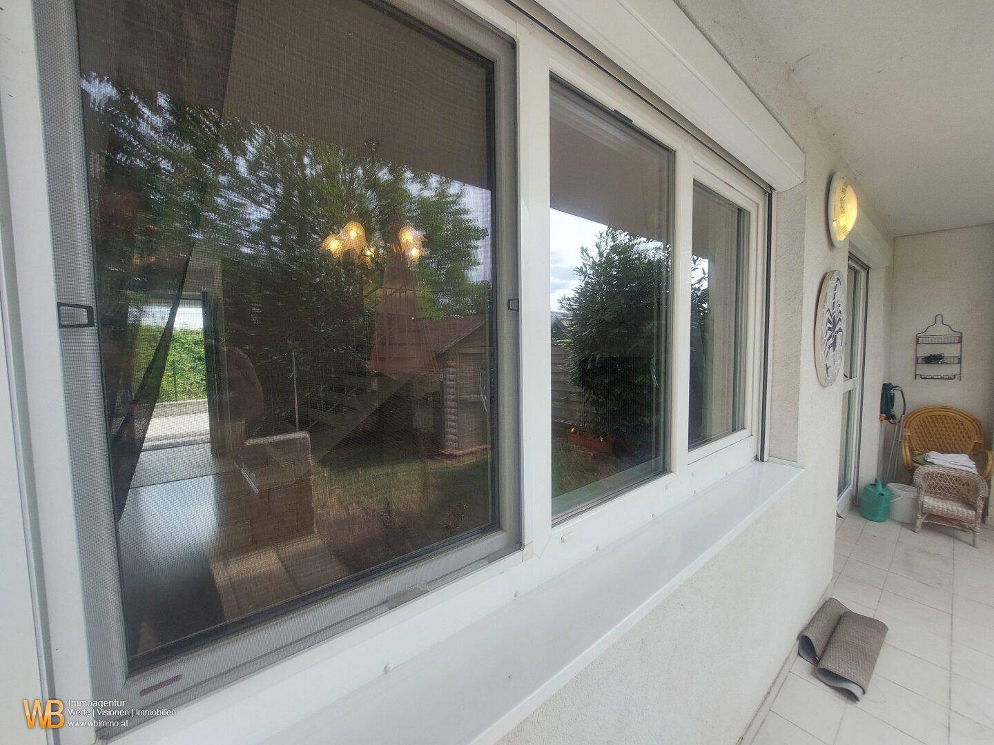 Fenster mit Rollladen und Blick auf den Garten mit Holzschuppen.