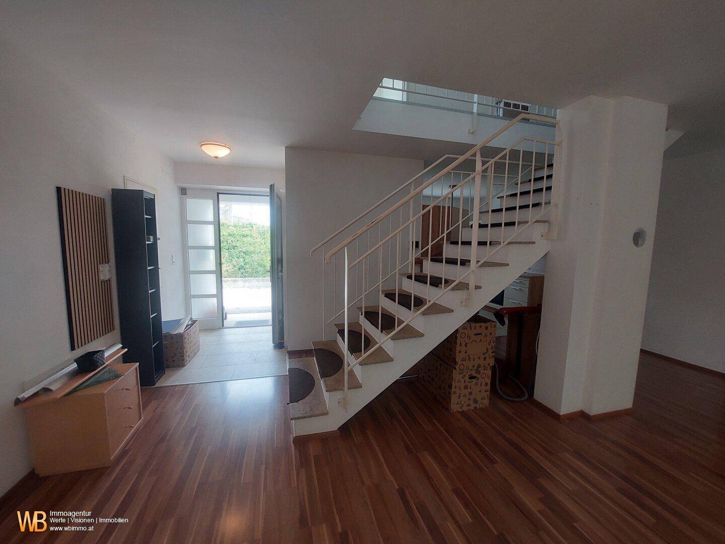 Wohnbereich mit Holzfußboden, Treppe und hellem Eingangsbereich.