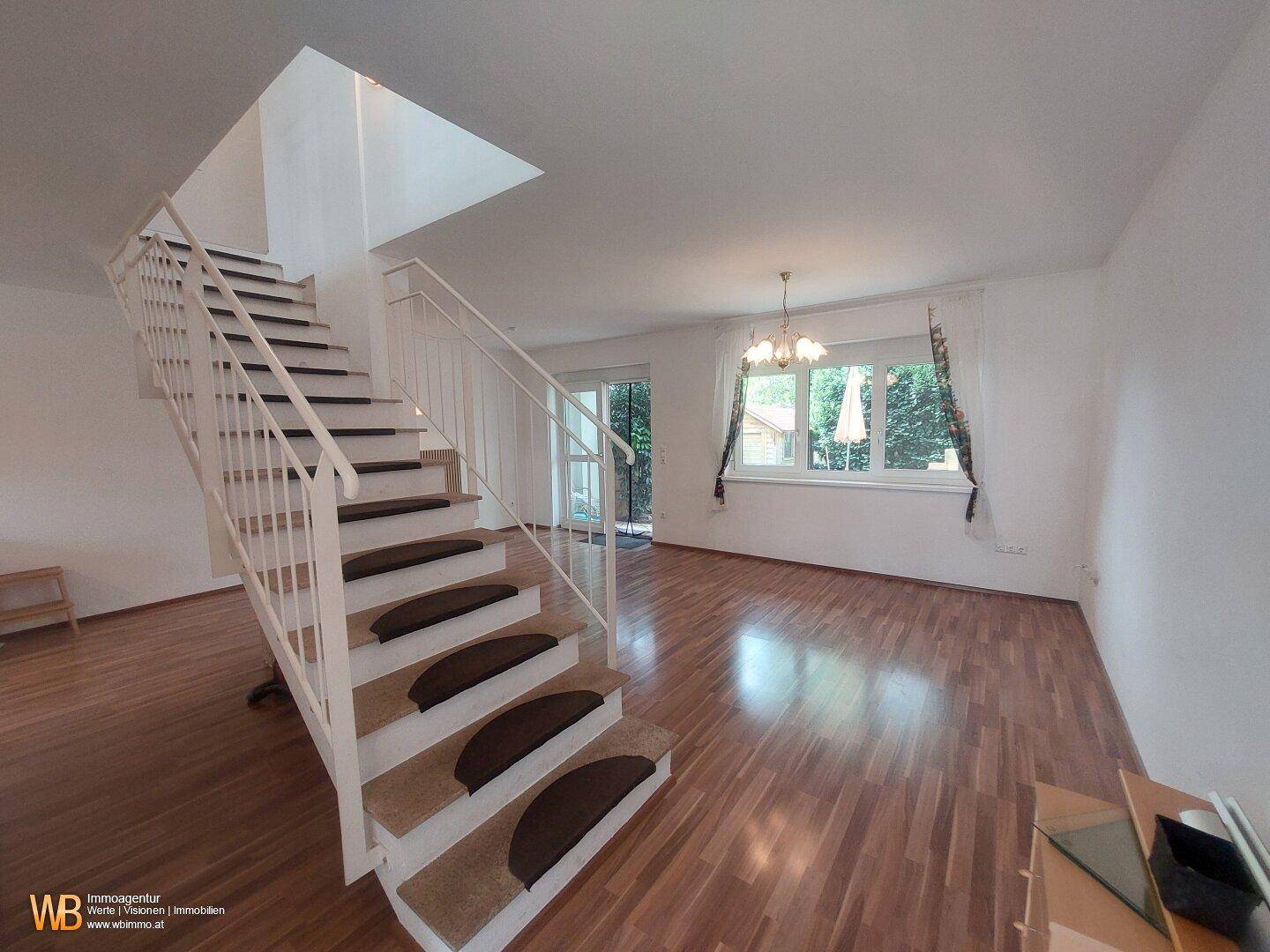 Geräumiger Wohnbereich mit offener Treppe, Holzfußboden und Zugang zur Terrasse.