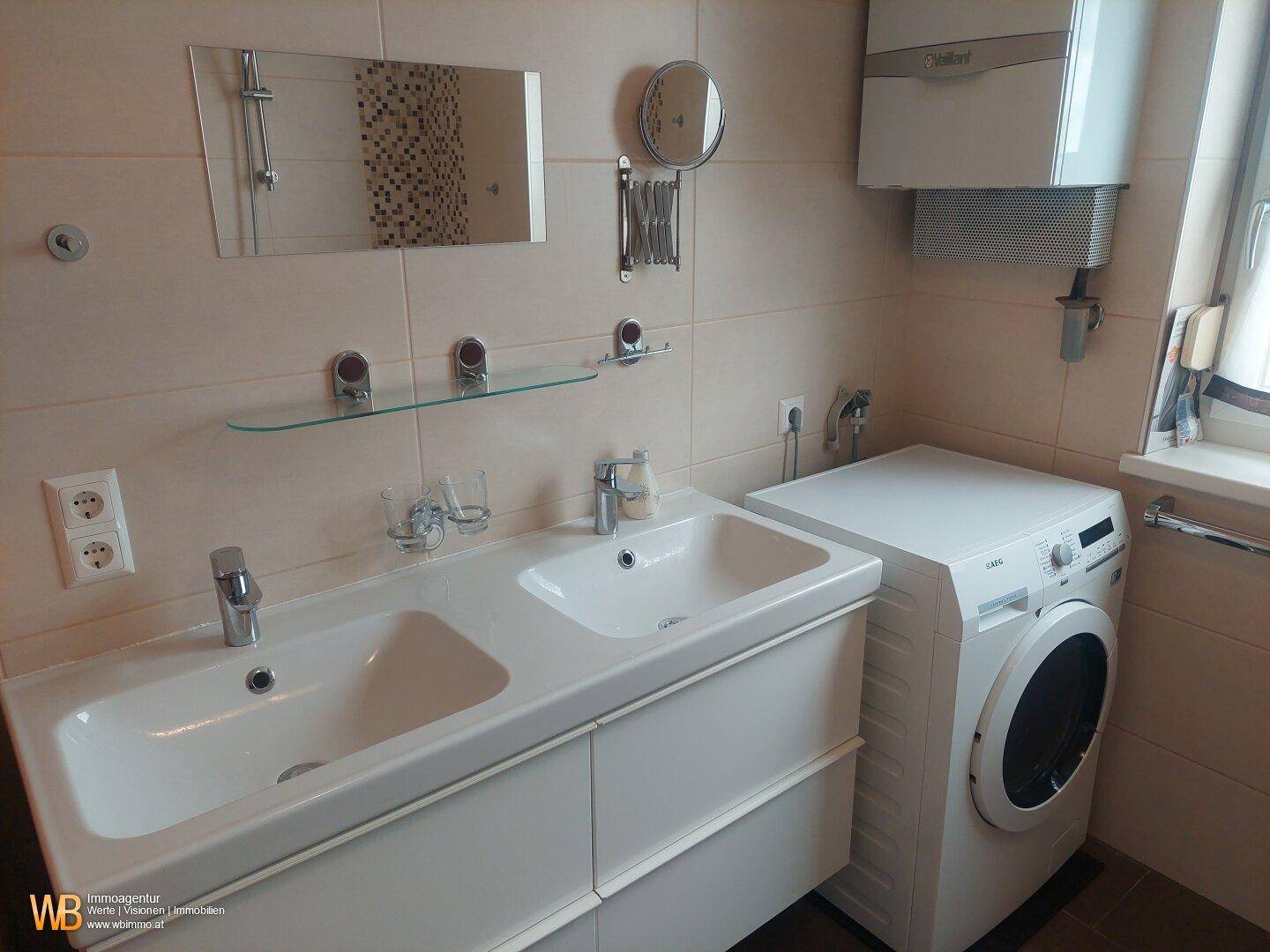 Badezimmer mit Doppelwaschbecken, Waschmaschine und Wandheizung.