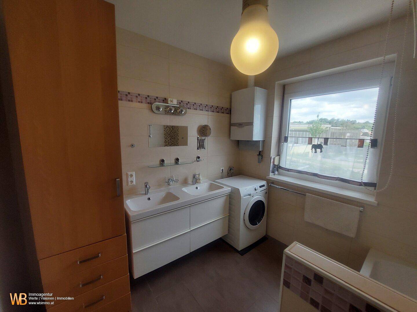Helles Badezimmer mit Fenster, Doppelwaschbecken und Waschmaschine.