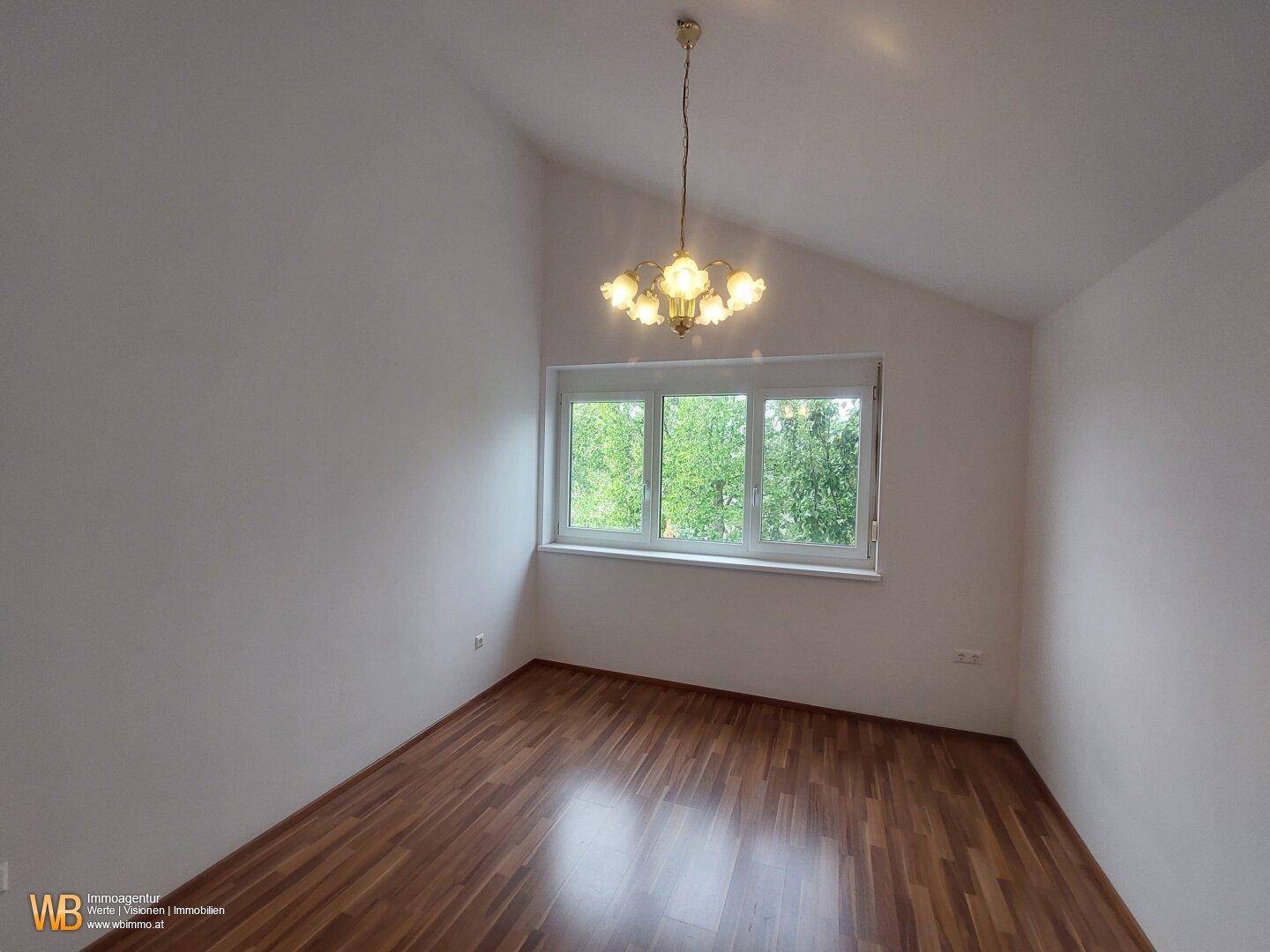Schlafzimmer mit Holzfußboden, großem Fenster und Dachschräge.