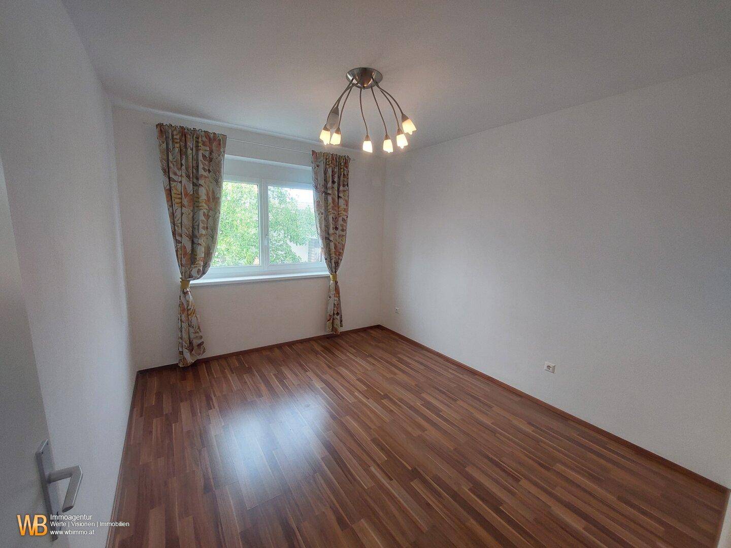 Helles Schlafzimmer mit Holzfußboden und Fenster mit Vorhängen.