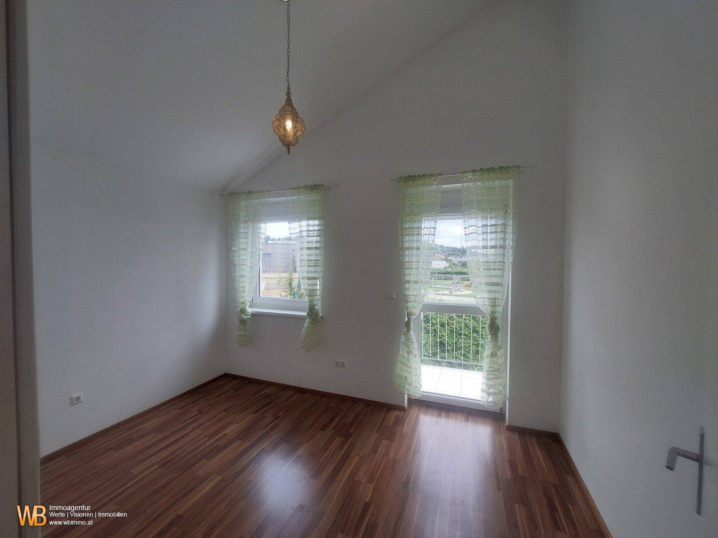 Schlafzimmer mit Holzfußboden, zwei Fenstern und Dachschräge.