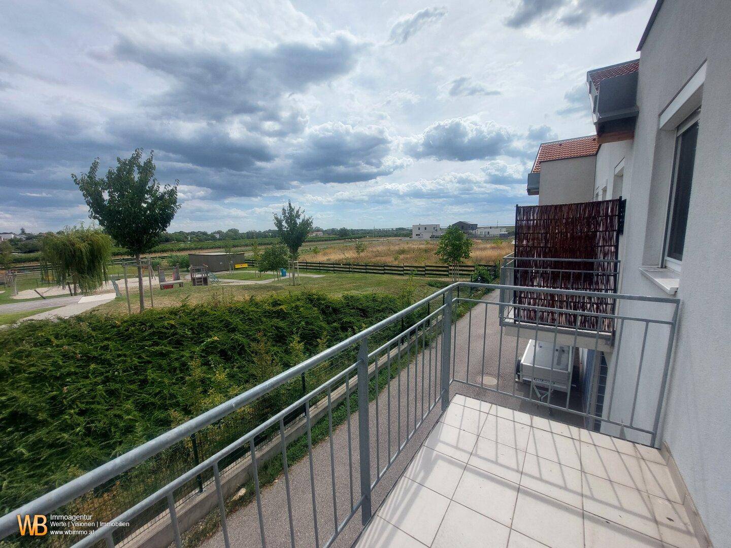 Balkon mit Blick auf die grüne Umgebung, Spielplatz und angrenzende Gebäude.