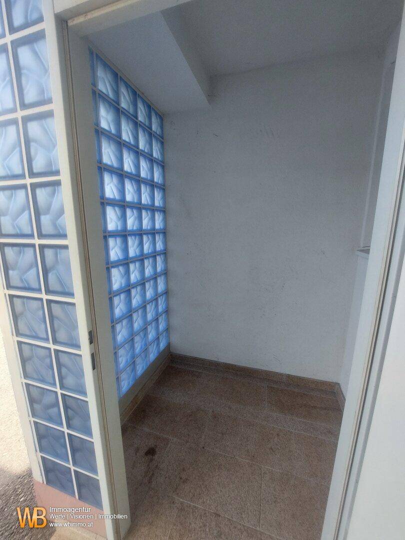 Kleiner Raum mit Glasbausteinwand, gefliestem Boden und begrenzter Sichtbarkeit.