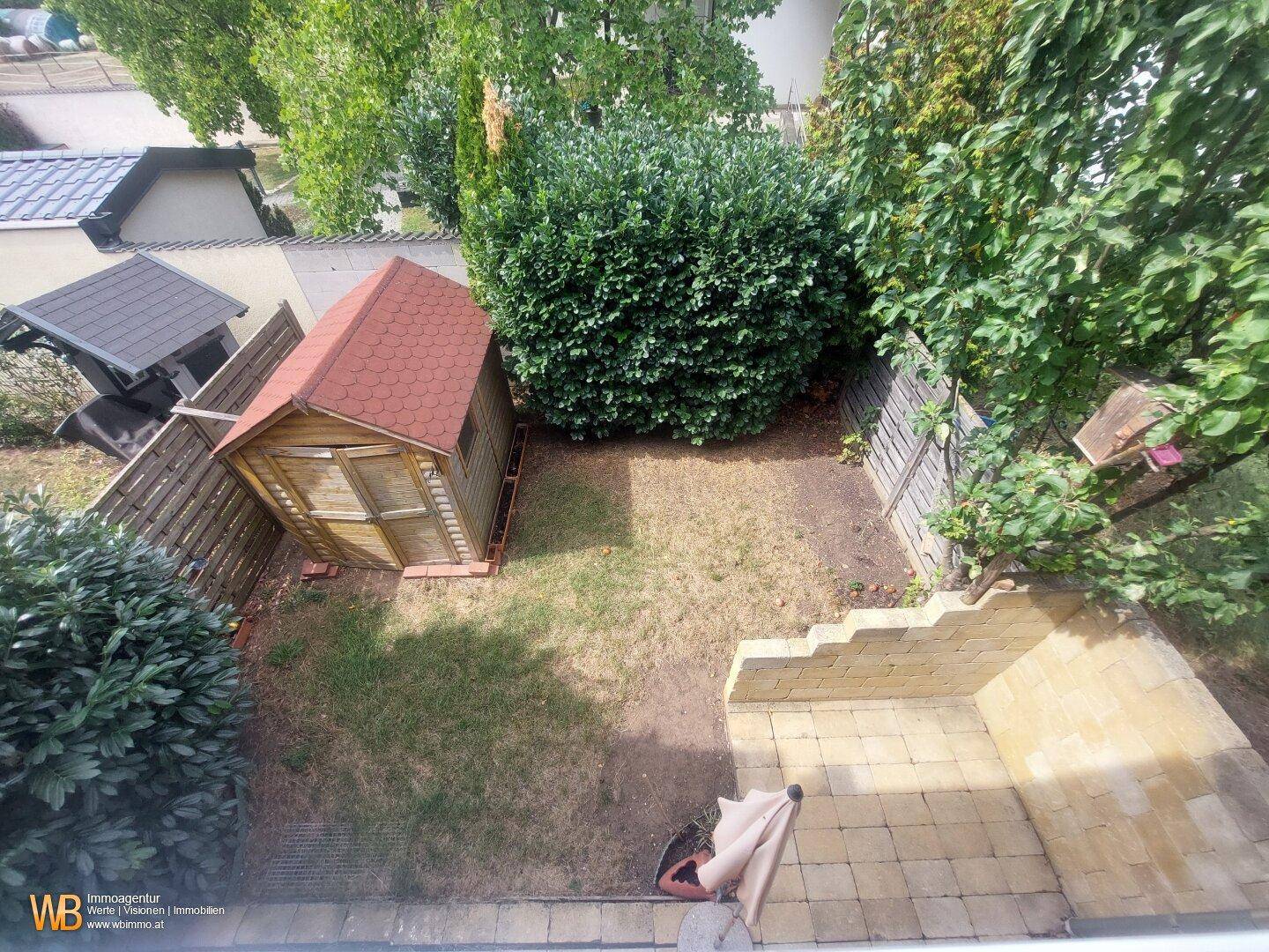 Vogelperspektive des Gartens mit Holzschuppen, Rasenfläche und Terrasse.