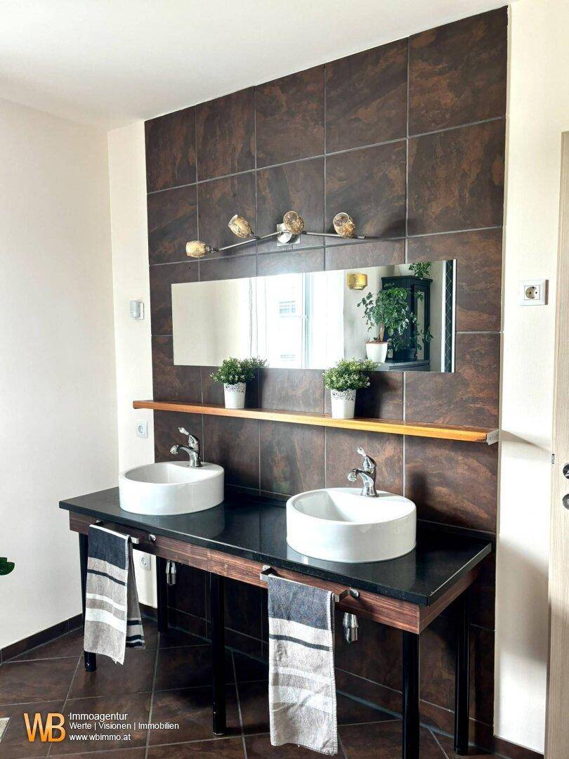 Modernes Badezimmer mit zwei stilvollen Aufsatzwaschbecken und dunklen Wandfliesen.