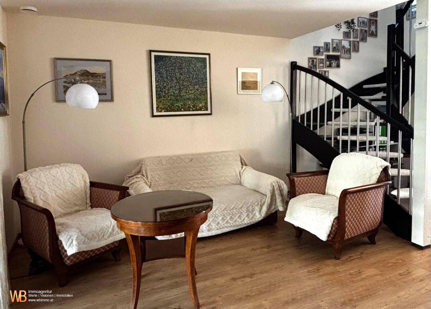 Gemütliches Wohnzimmer mit traditionellen Möbeln, Holzboden und einem eleganten Treppenaufgang.